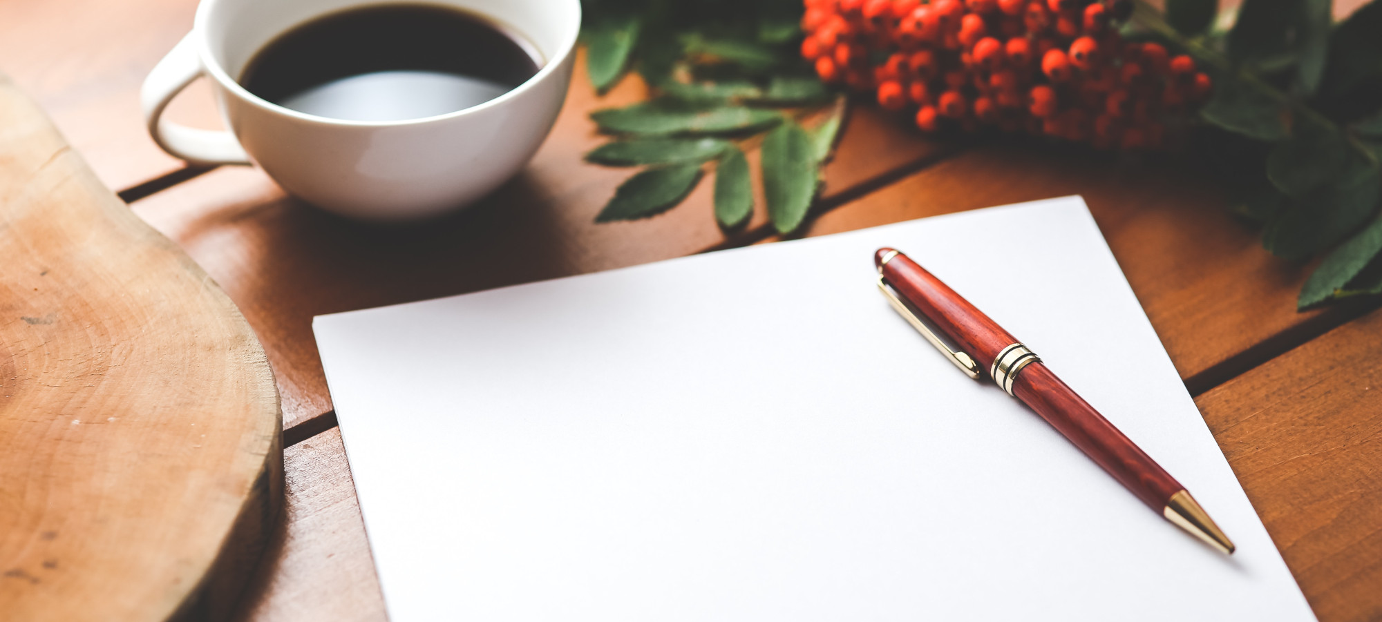 A stylish pen on top of a notebook next to a cup of coffee on a wooden table